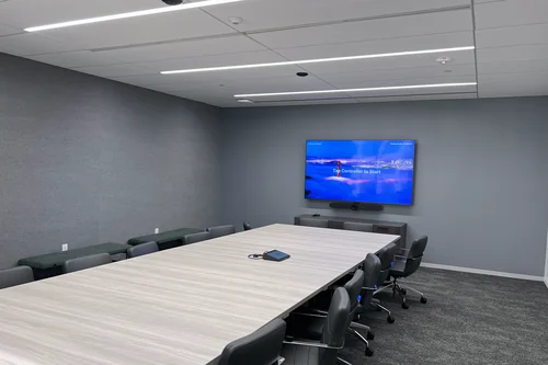 A long conference room with a wall display and video bar at the far end, and a cable ingest puck part way down the table.