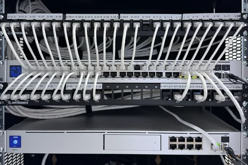A network rack: two patch panels labelled by floor and by access point, patched to a switch above a UniFi Dream Machine Pro.
